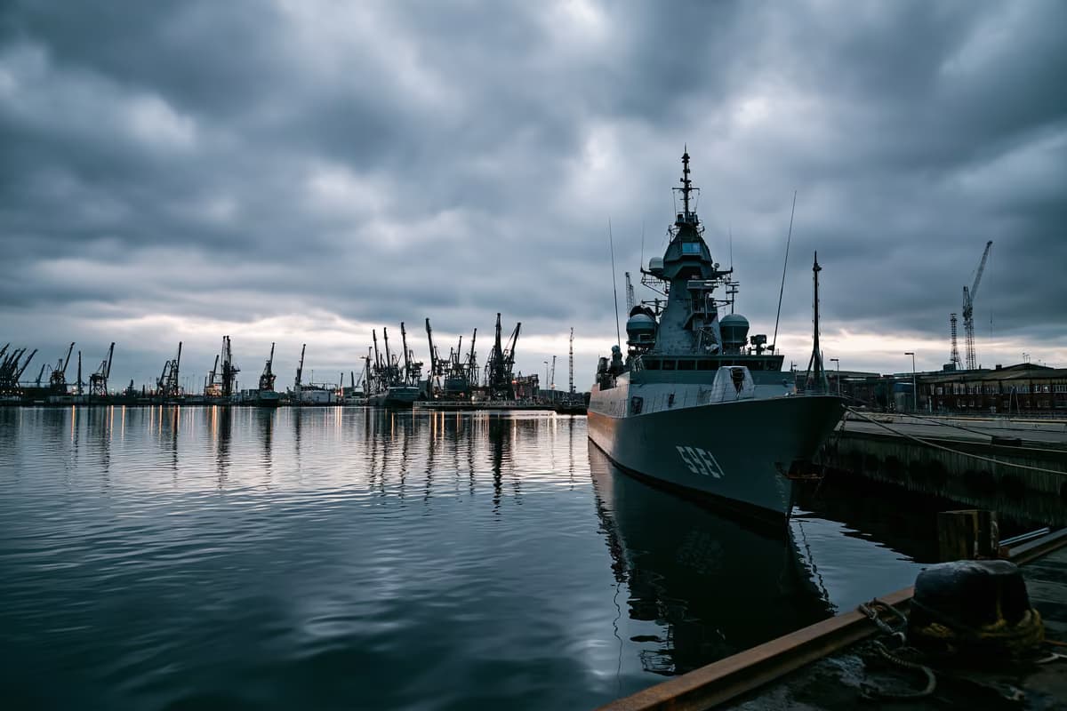 Szara stocznia marynarki wojennej pod zachmurzonym niebem, co sugeruje inwestycje w obronność.