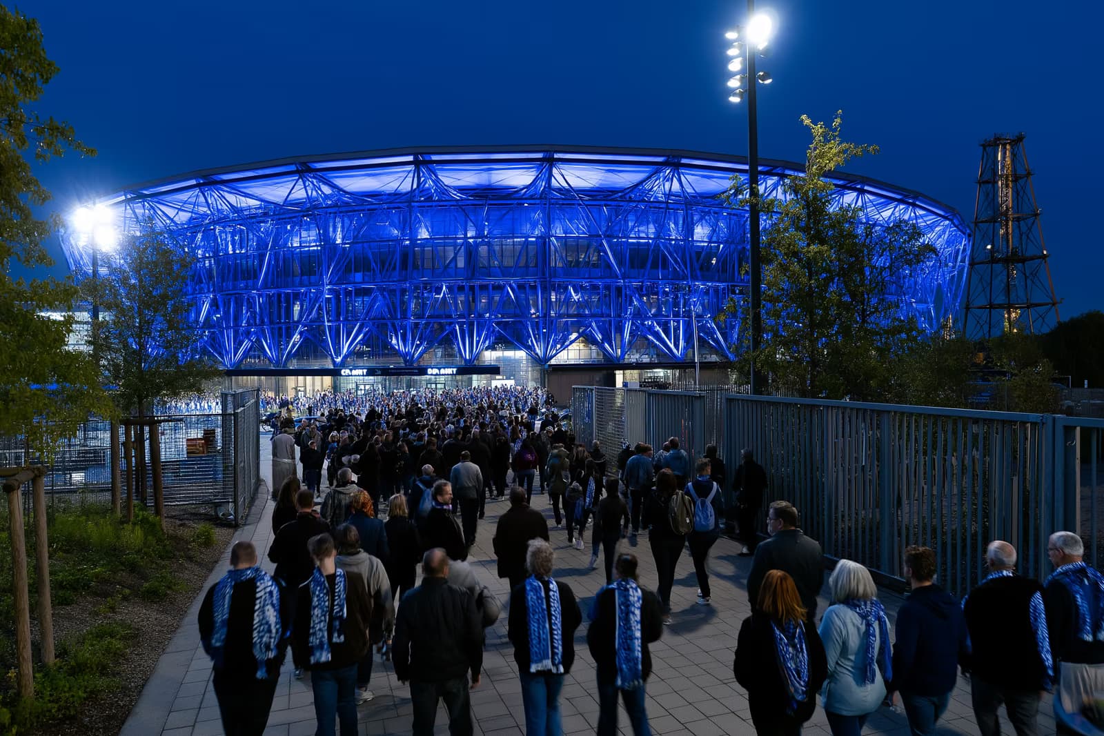 Stadion piłkarski w Zagłębiu Ruhry nocą lśni królewsko niebieskim blaskiem, gdy kibice w szalikach gromadzą się w kierunku bram po meczu Gosens Schalke