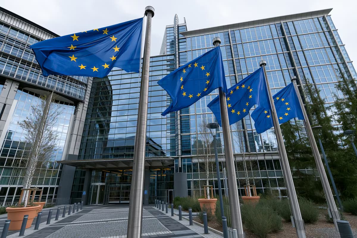 Flagi Unii Europejskiej na masztach przed nowoczesnym szklanym budynkiem.